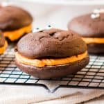 Close up of chocolate whoopie pie with orange filling on a black wire rack.