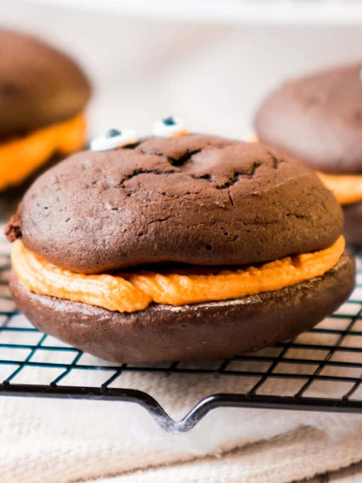 Close up of chocolate whoopie pie with orange filling on a black wire rack.