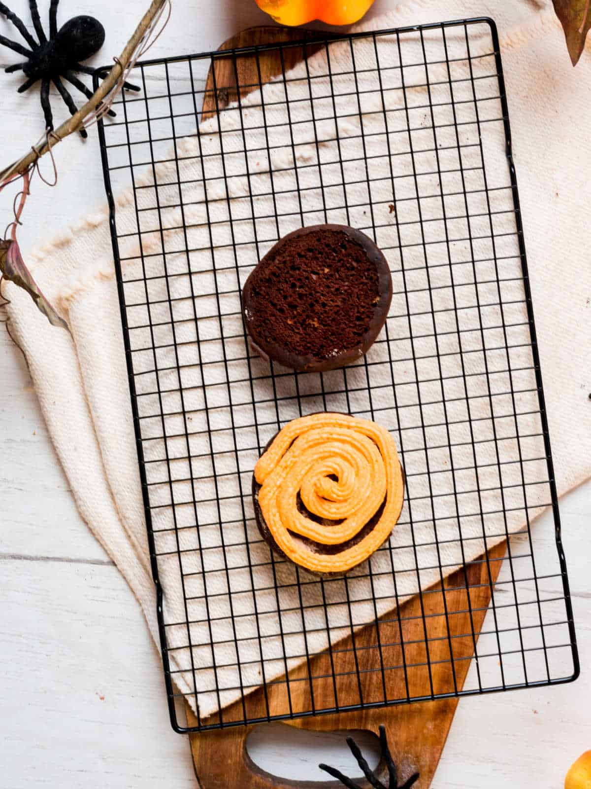 Black wire rack with two chocolate soft cookies; one has an orange filling.
