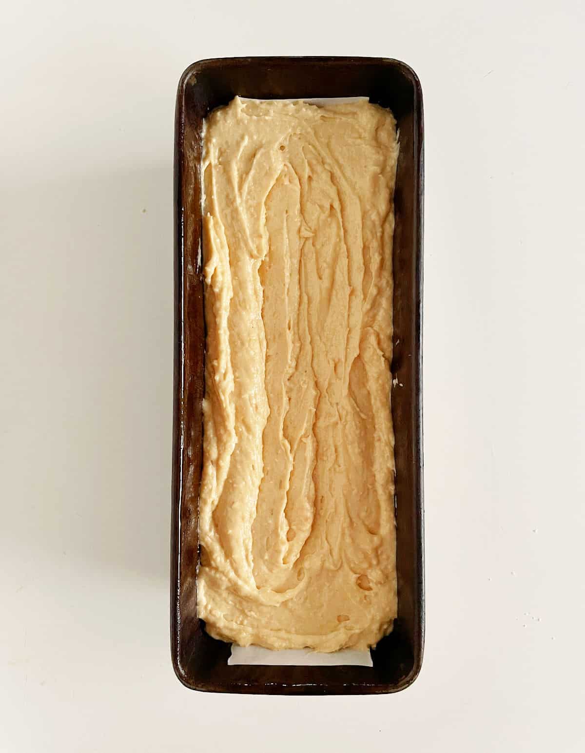 Hazelnut cake batter in a dark loaf pan on a white surface.