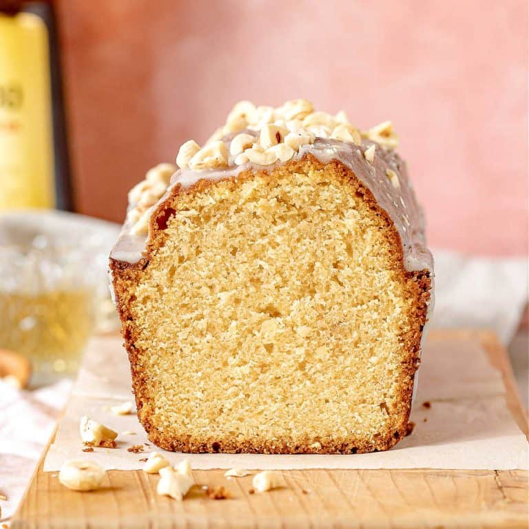 Front view of cut hazelnut pound cake on a wooden board with parchment paper and pink background.