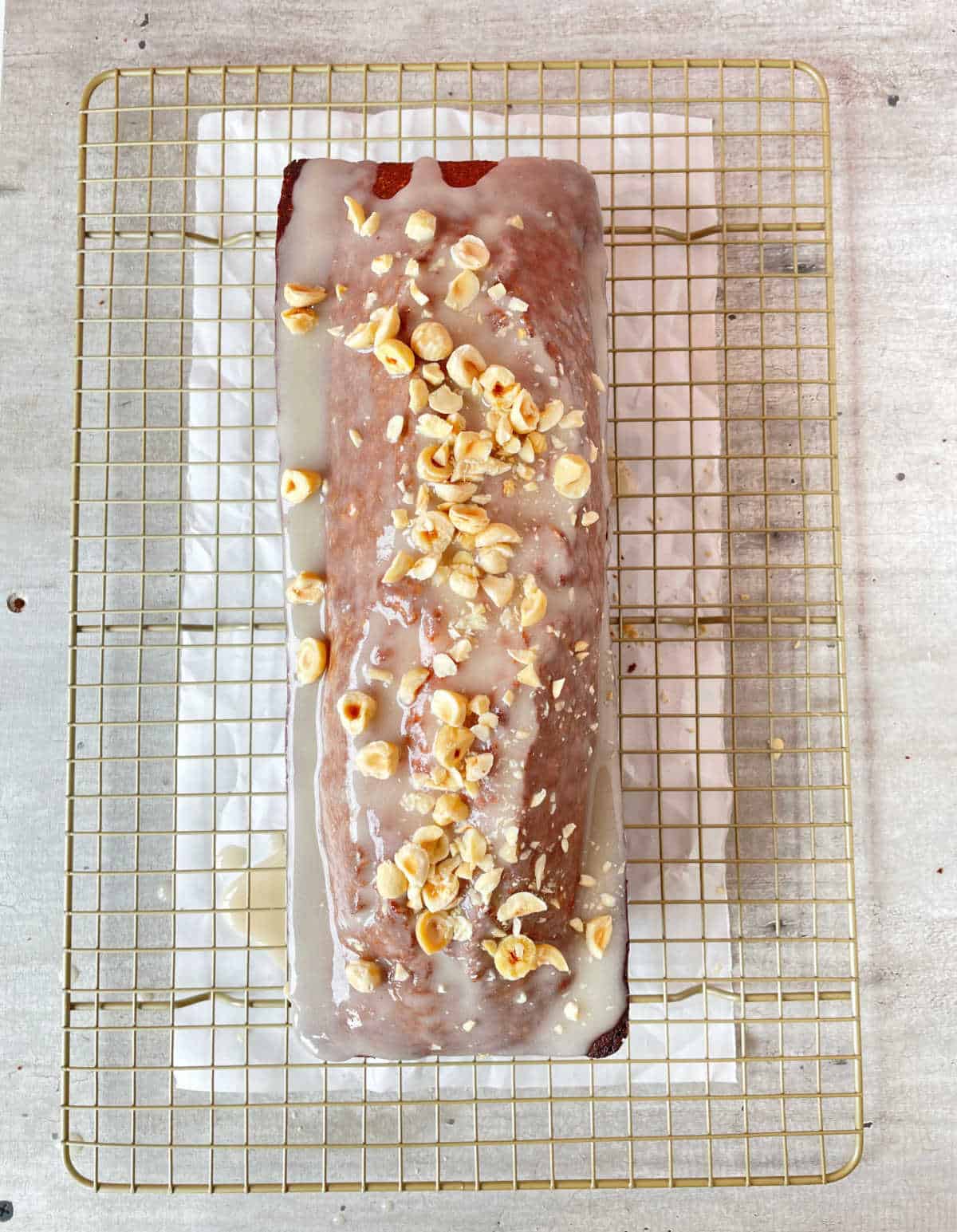 Glazed pound cake with chopped hazelnuts on a wire rack with parchment paper. Grey surface.