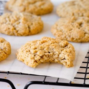 Close up image of bitten oatmeal cookie on white paper on a black wire rack with whole cookies behind.