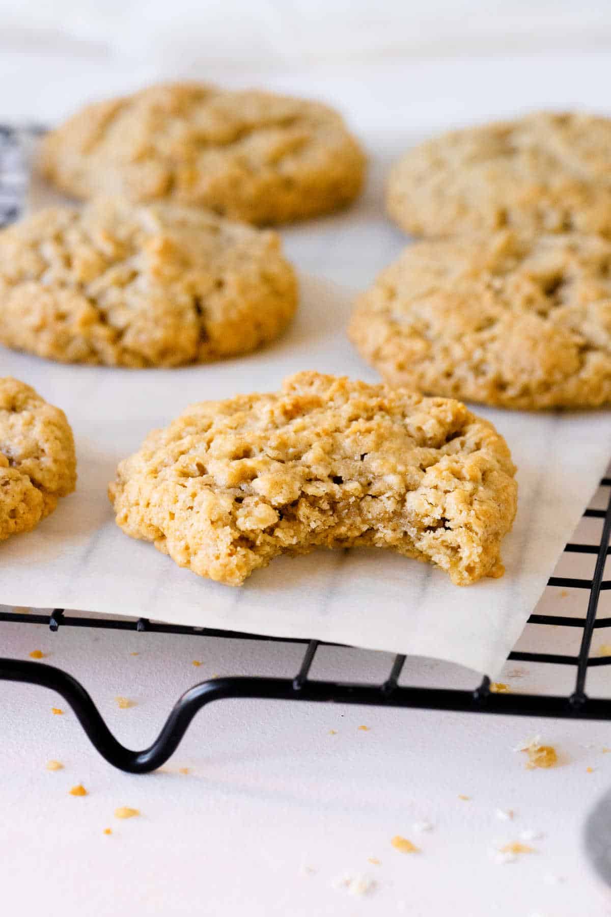 Bitten oatmeal cookie with several whole ones on parchment paper on a black wire rack.