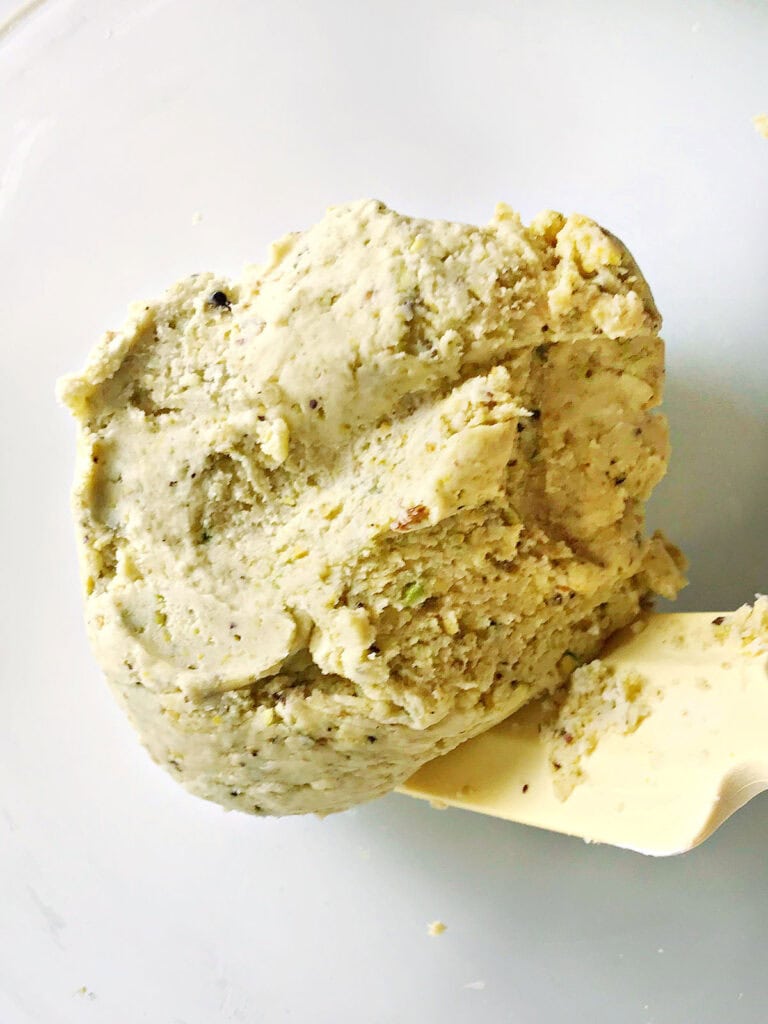 Final pistachio cookie dough on a white surface. Yellow spatula.