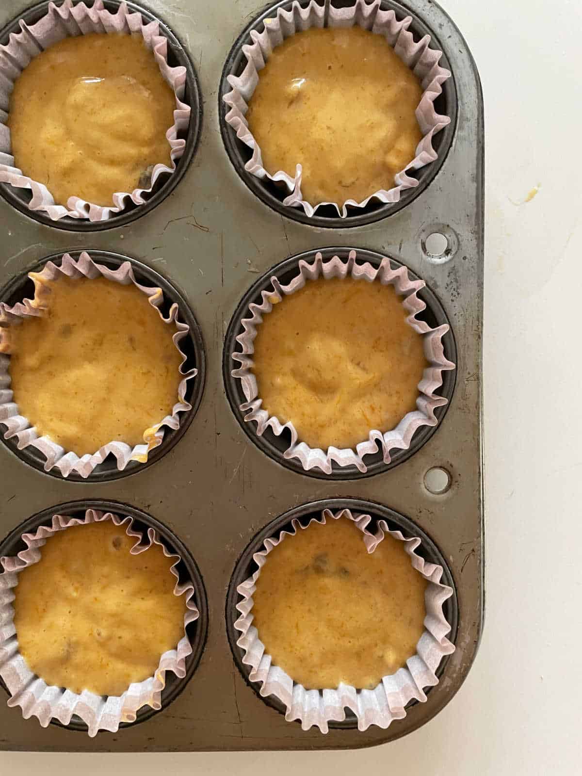 Metal muffin tin with unbaked pumpkin muffins with paper liners. White surface.