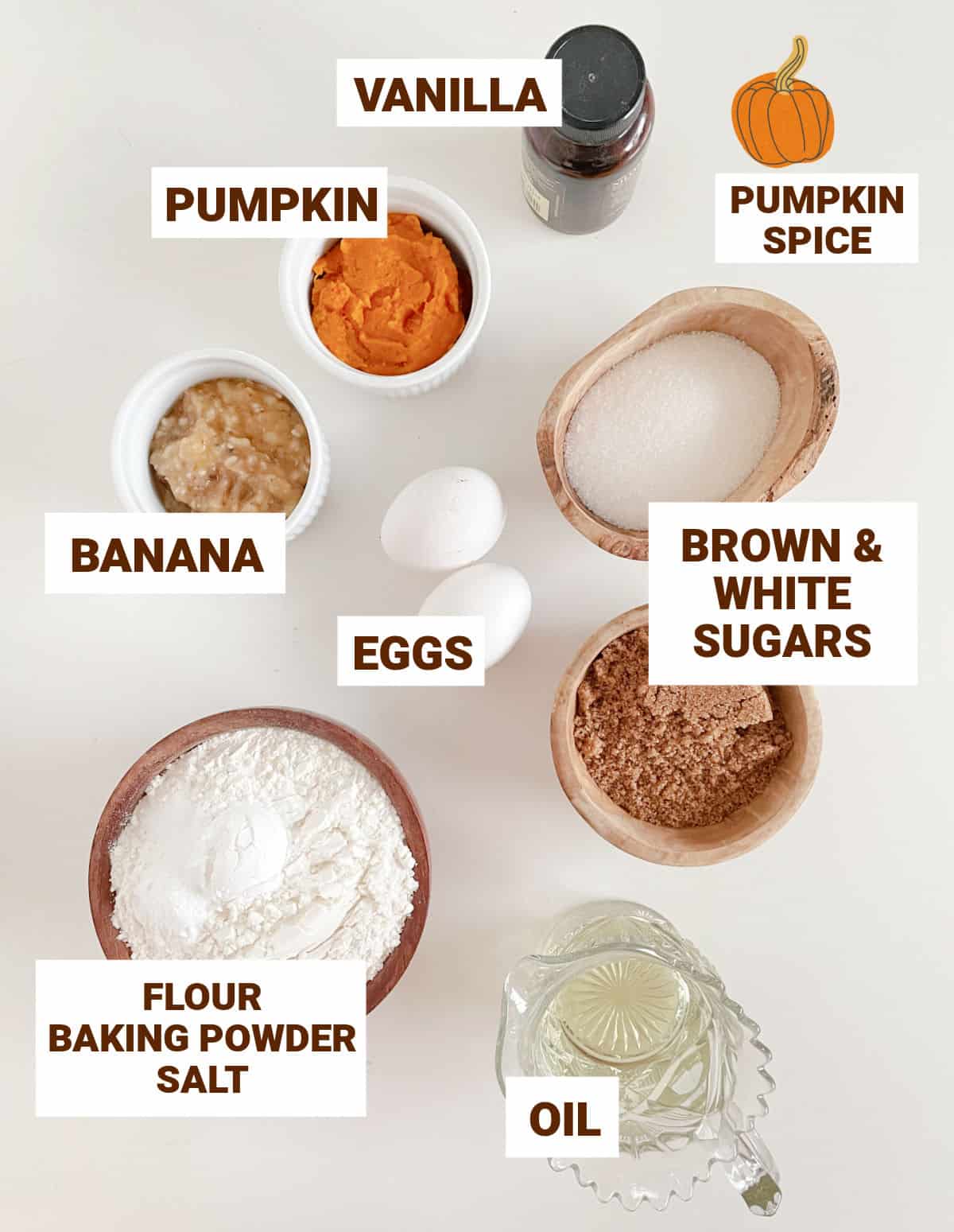 Bowls with ingredients for pumpkin banana muffins on a white surface including oil, sugars, flour, eggs, flavorings.