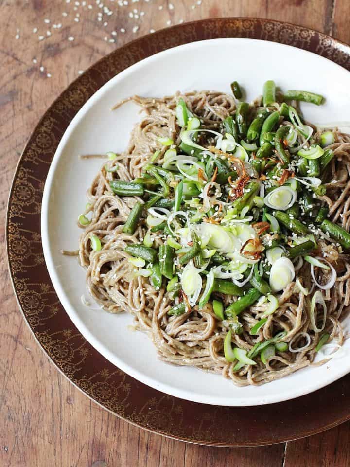 Soba noodle salad topped with green beans on white plate, wooden table.