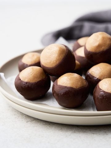 Two stacked white plates with several buckeyes. White background and grey cloth.