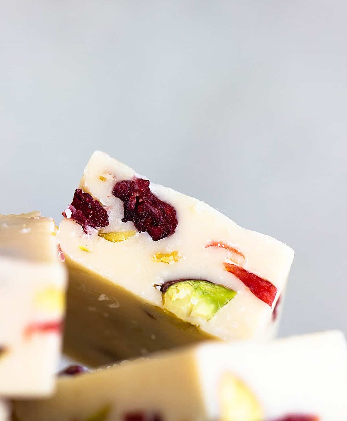 Close-up image of piece of white fudge with cranberries and pistachios, grey background.