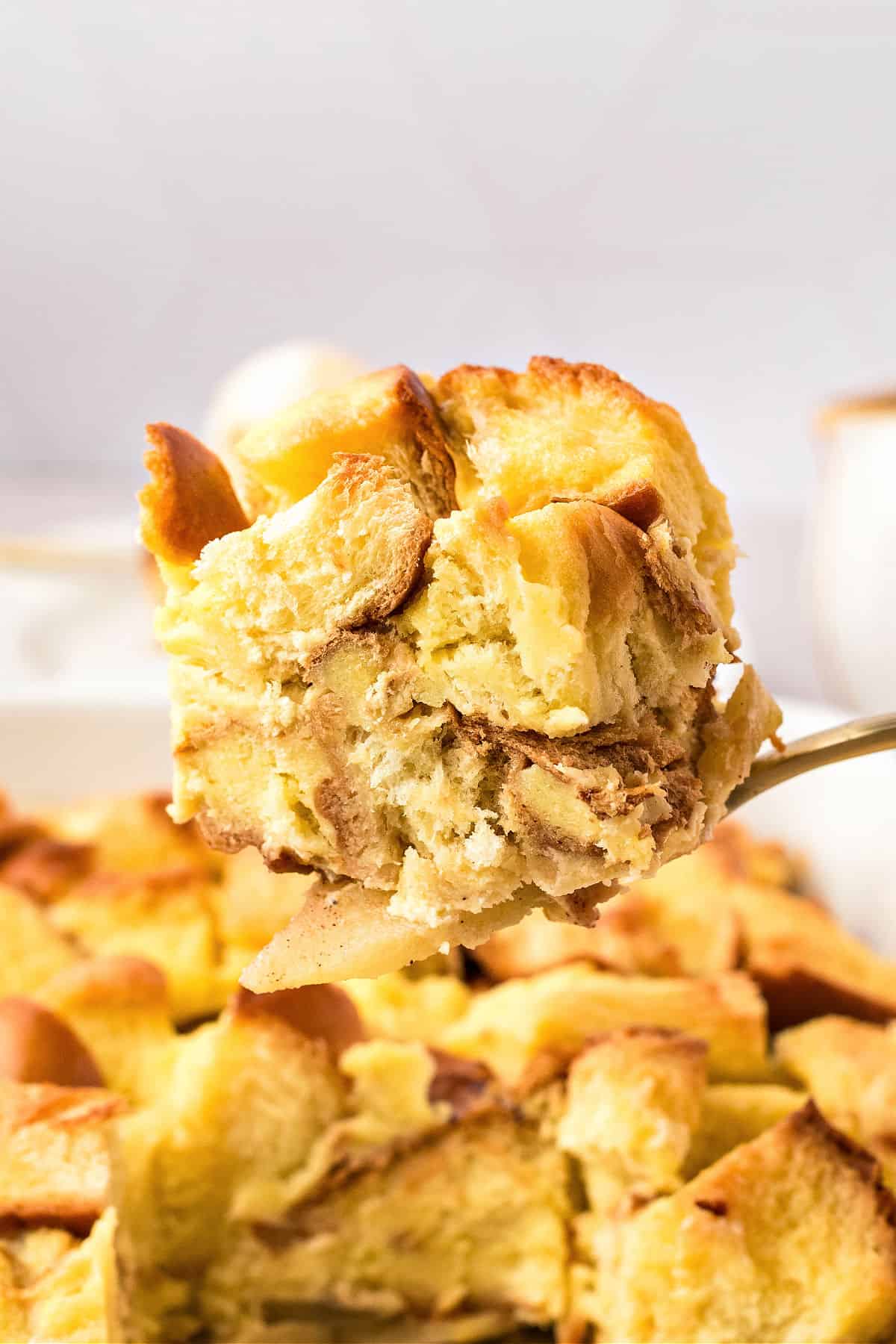 Lifting a serving of apple bread pudding from dish. Light gray background.