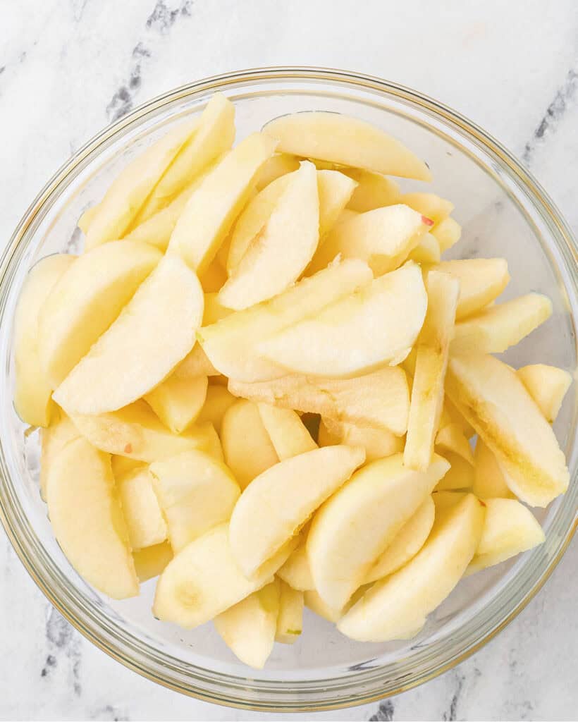 Glass bowl of sliced fresh Granny Smith apples before cooking.