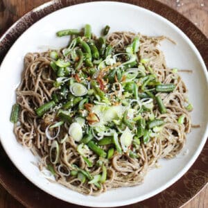 Top view of white plate with soba noodle green bean salad on a wooden table.