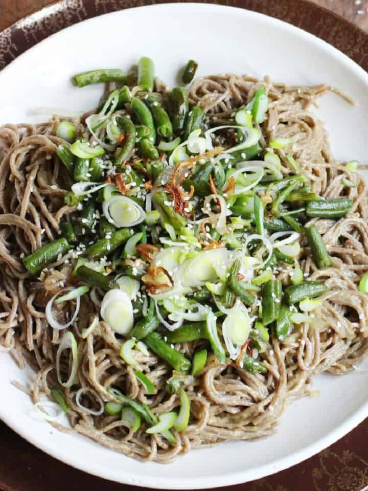 Top view of white plate with soba noodle green bean salad on a wooden table.