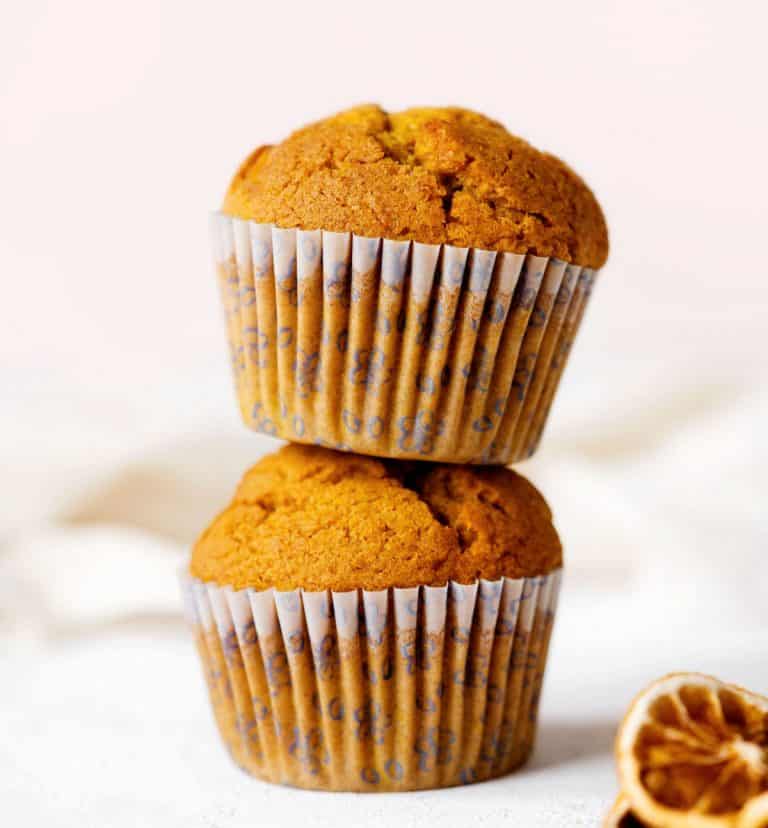 Close up image of two stacked pumpkin muffins on a white surface with pink background.