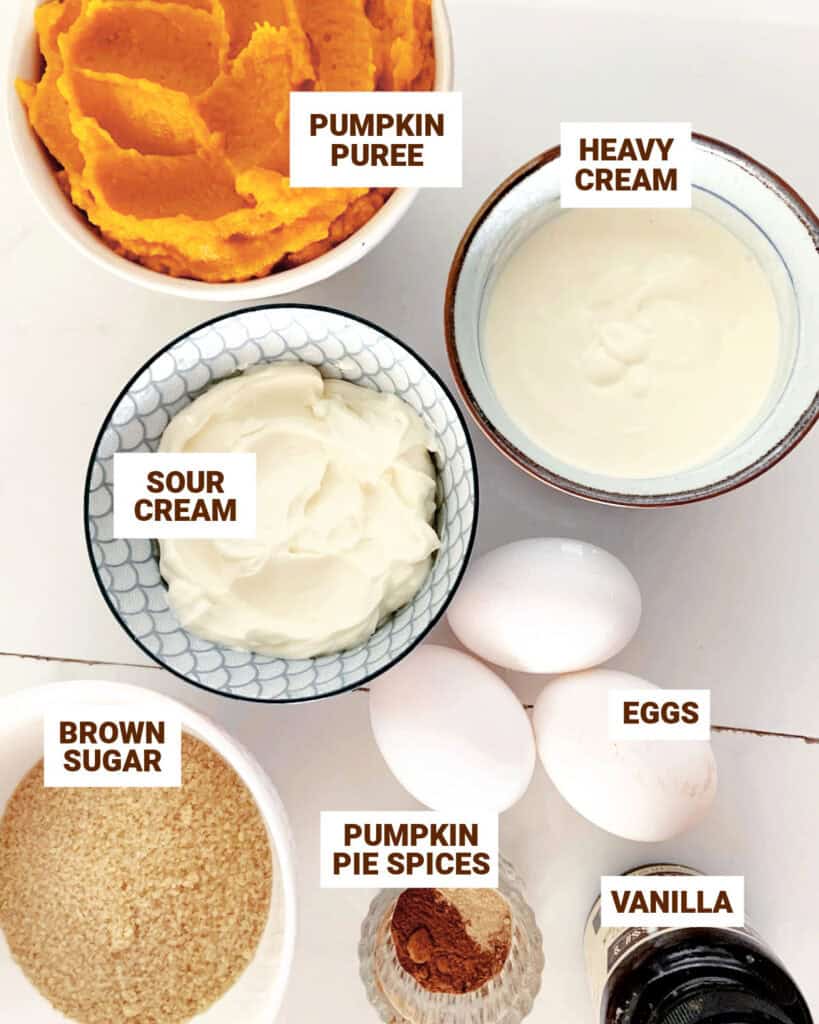 White surface with bowls containing ingredients for pumpkin pie with sour cream and brown sugar.