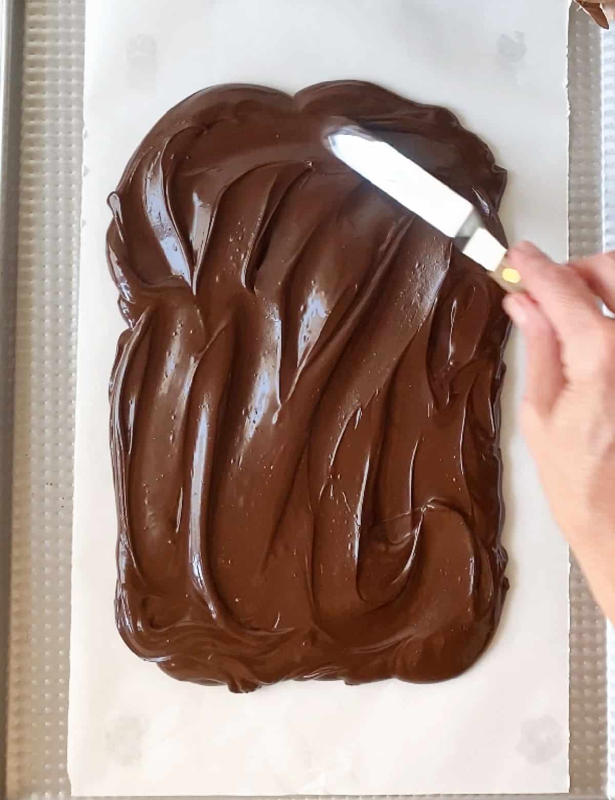 Spreading dark chocolate with an offset spatula on a white piece of paper. Top view.