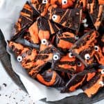 Pieces of dark and orange halloween bark with candy eyes on a metal plate with white paper.