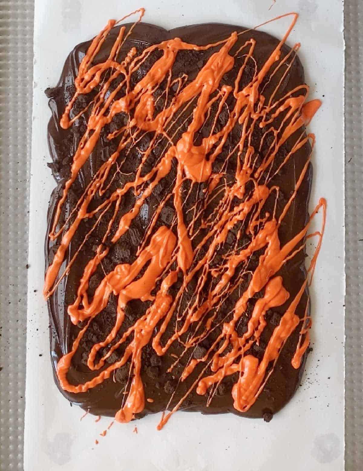 Orange colored chocolate drizzled over melted dark chocolate on a white piece of parchment paper. View from above. 