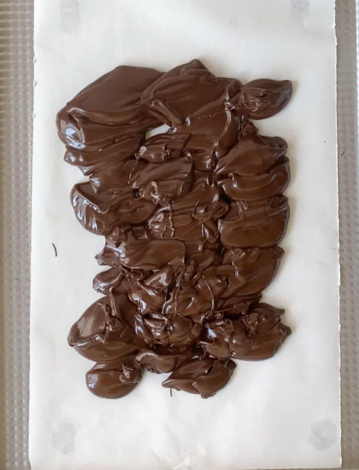 Melted dark chocolate in the middle of a piece of white parchment paper.