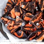 Orange and black text overlay on image of dark and orange chocolate bark with candy eyes.
