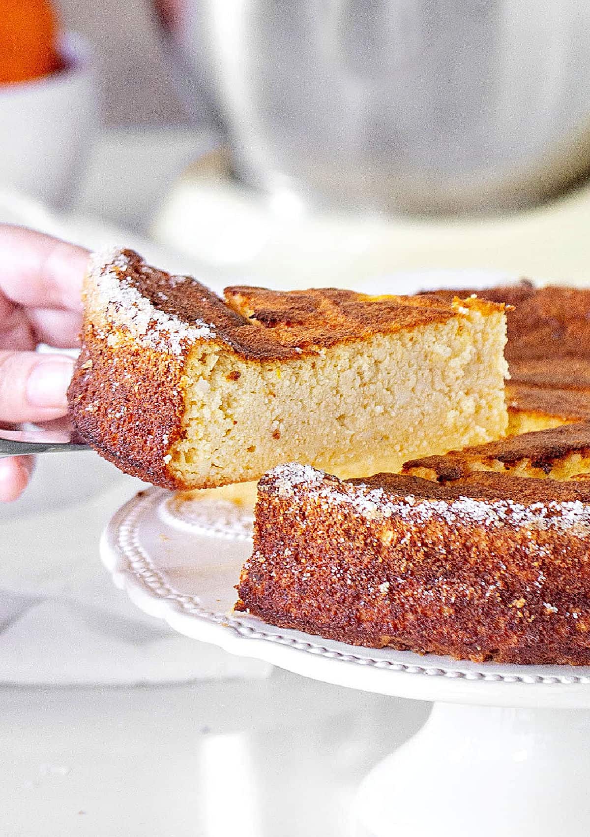 Creamy slice of crustless burnt ricotta cheesecake being lifted from cake on a white cake stand.