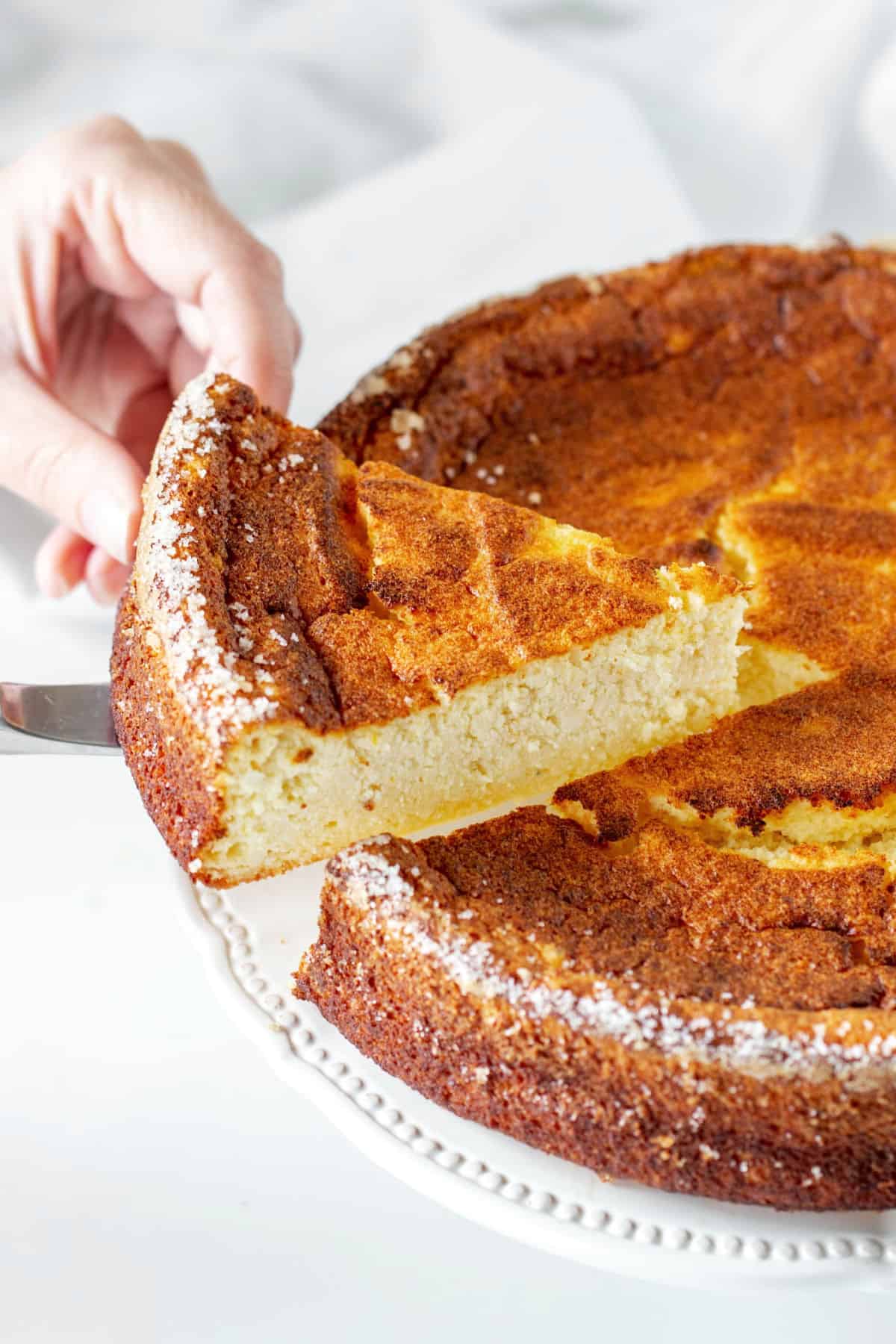 Whole Orange ricotta cheesecake and slice being cut Lifting a slice from whole crustless ricotta cheesecake. White plate and background.