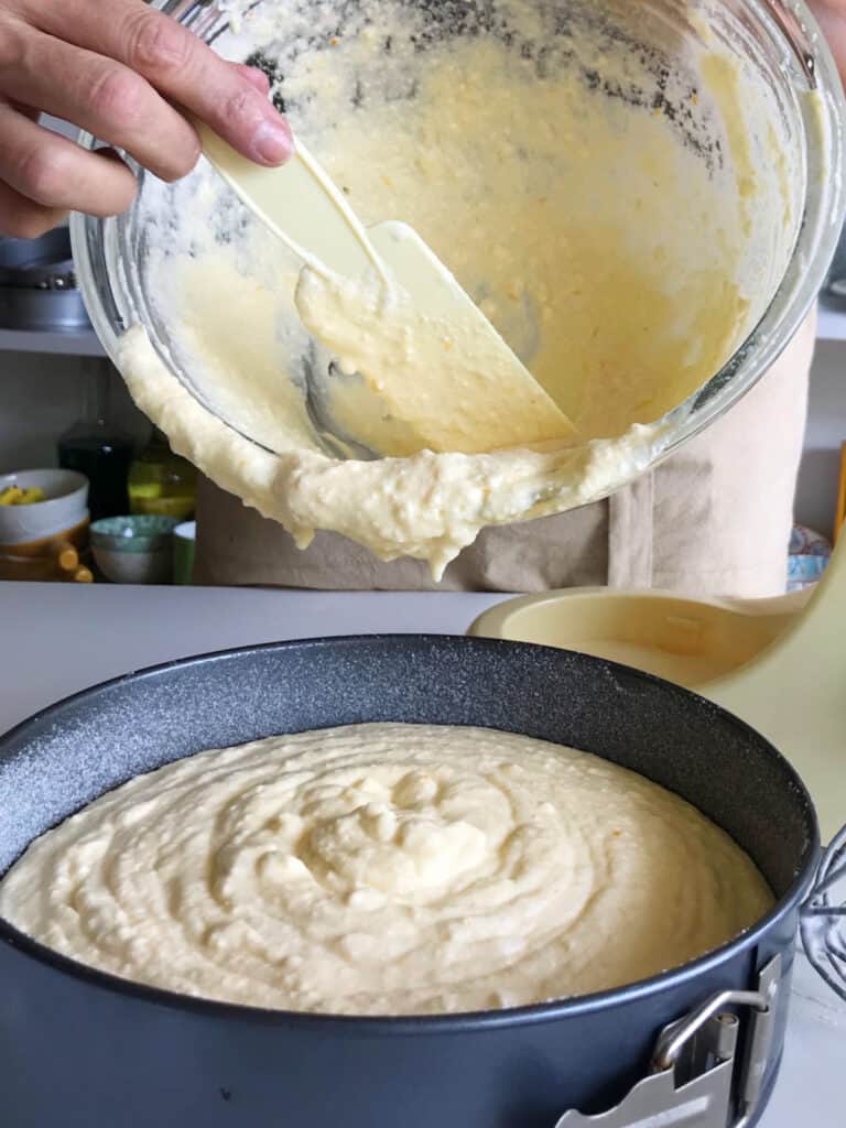 Pouring ricotta cheesecake batter from a glass bowl onto a springform pan.