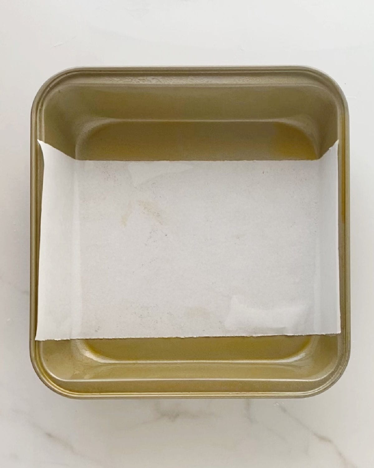 Square metal pan lined with strip of parchment paper. White surface.