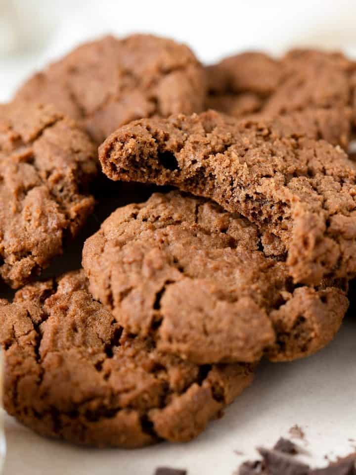A pile of chocolate cookies, top one is bitten on a white surface and background.