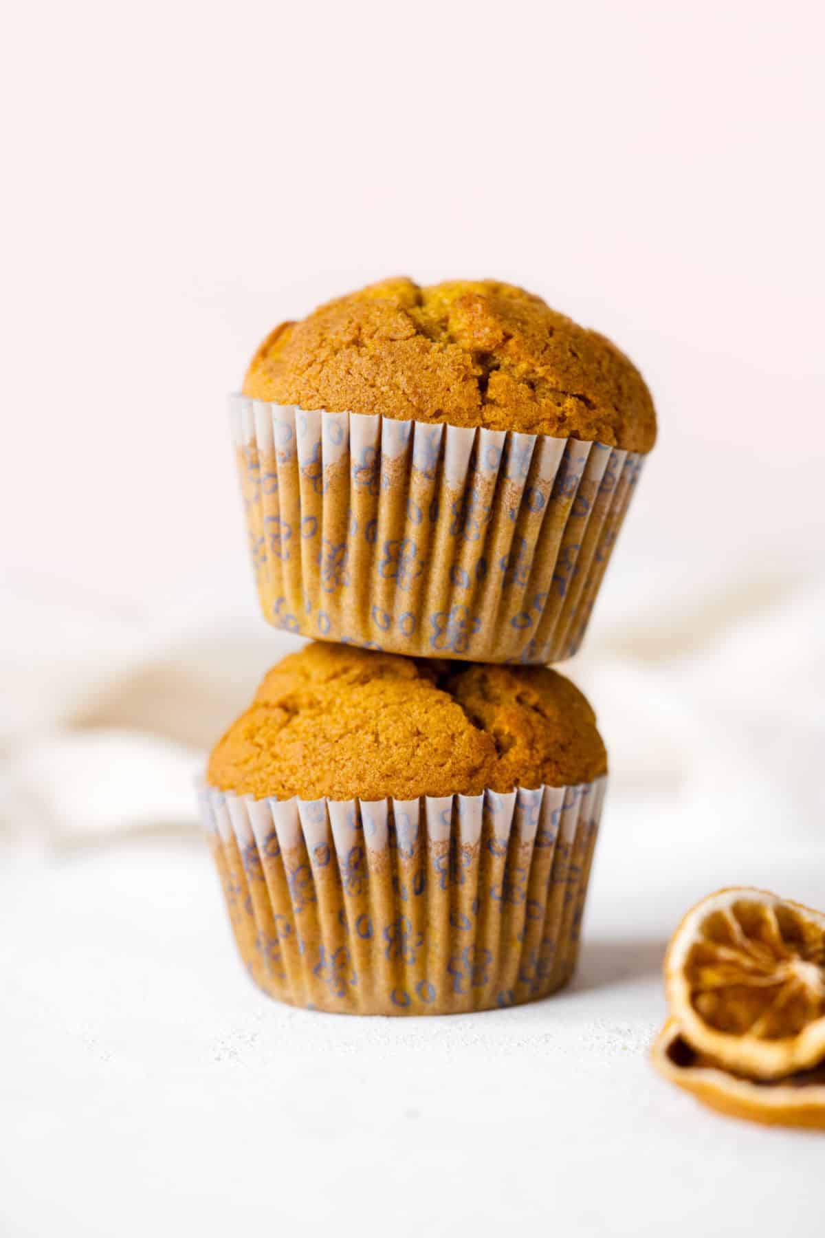 Two pumpkin muffins stacked on a white surface with pink background. 