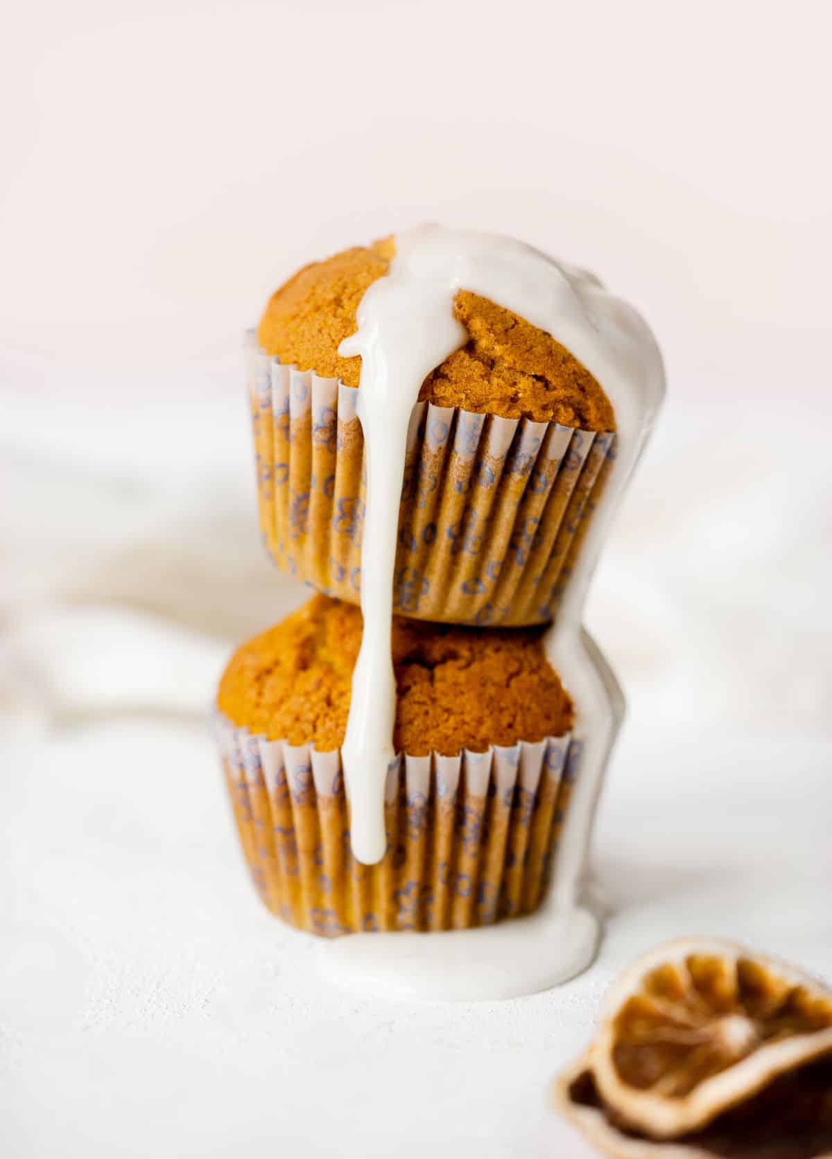 Glaze dripping down two stacked pumpkin muffins. White surface and pink background. 