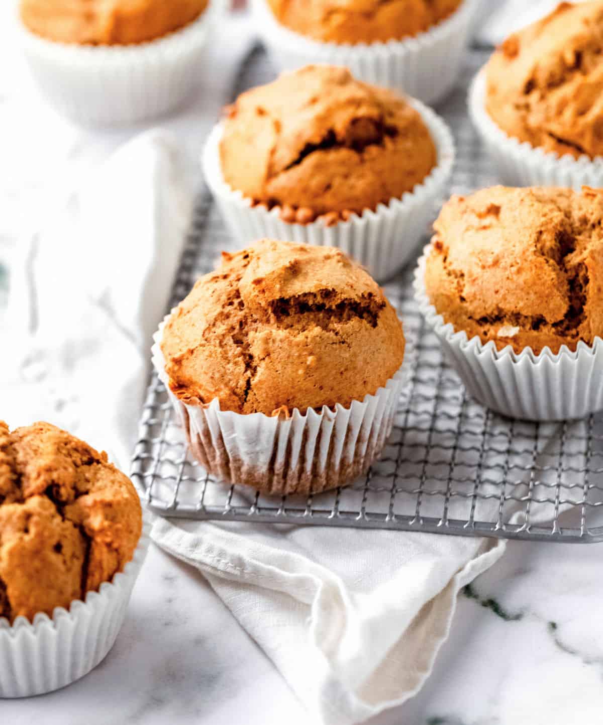 Several pumpkin muffins on a wire rack with a white cloth. White marble surface.