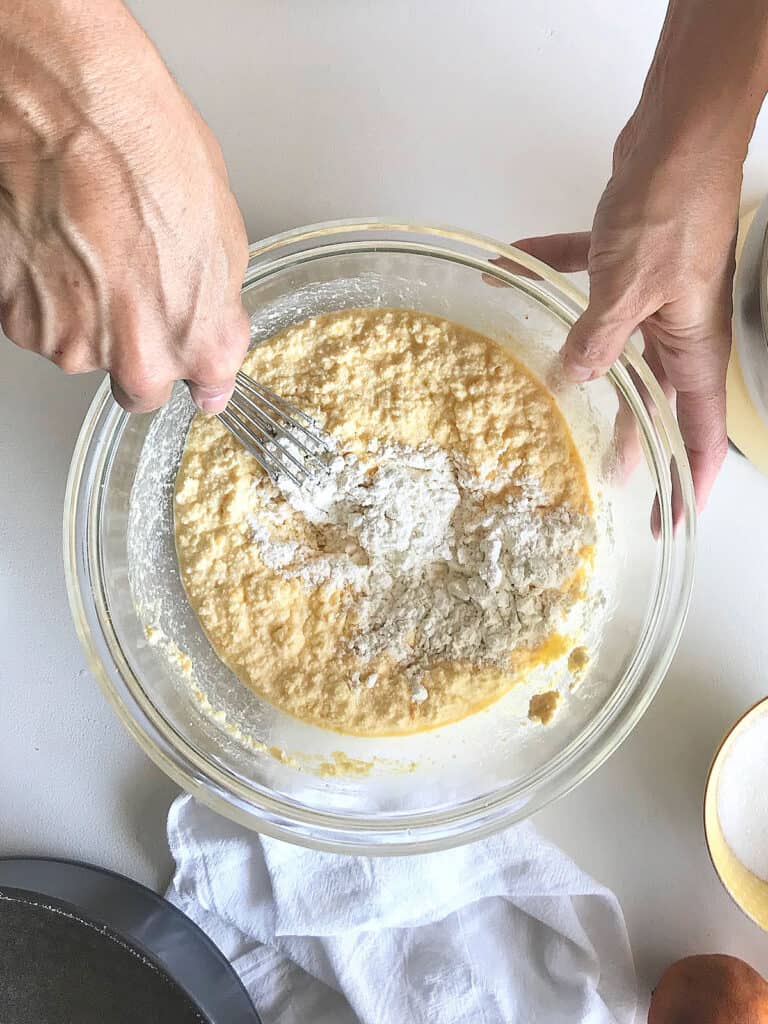 Mixing ricotta cheesecake batter in a glass bowl. White surface, top view.