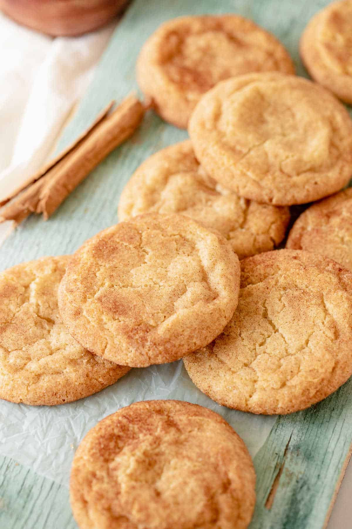 Several snickerdoodle cookies piled on a green wooden surface. A cinnamon stick beside them. 