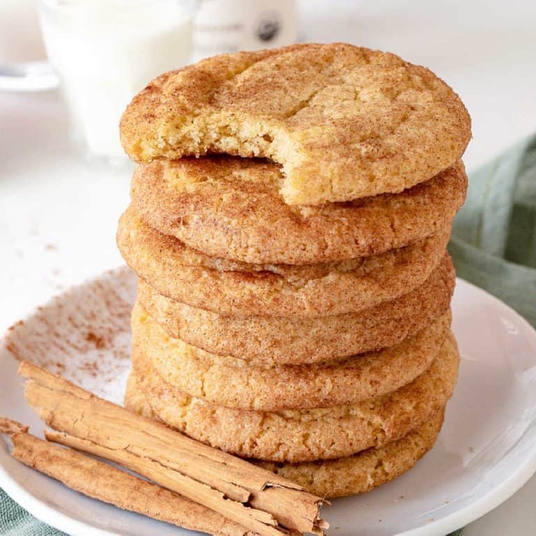 White plate with cinnamon sticks and stack of snickerdoodle cookies, top one bitten.