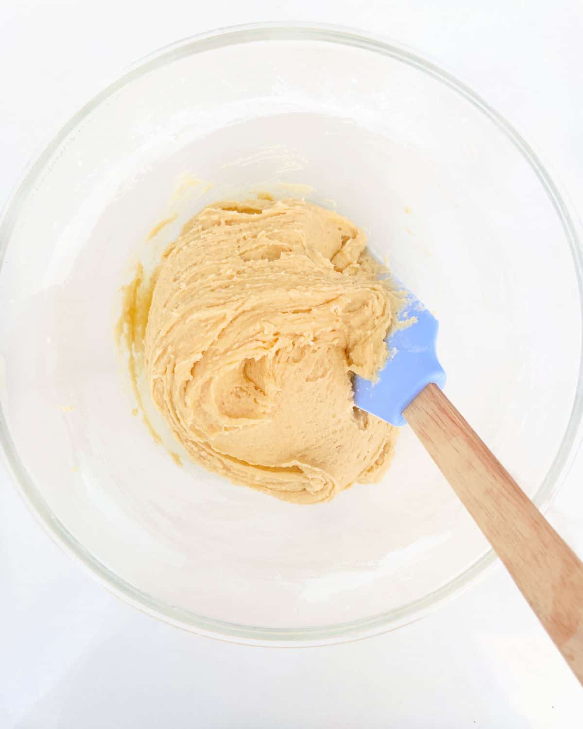 Snickerdoodle cookie dough in a glass bowl with a light blue spatula. White surface. Top view.