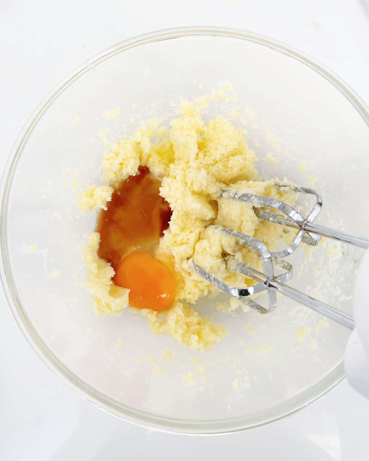 Glass bowl on a white surface containing butter and sugar mixture with cinnamon and eggs. Electric mixer inside.