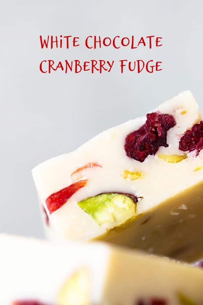 Red text overlay over close up image of pistachio cranberry white fudge with a grey background.