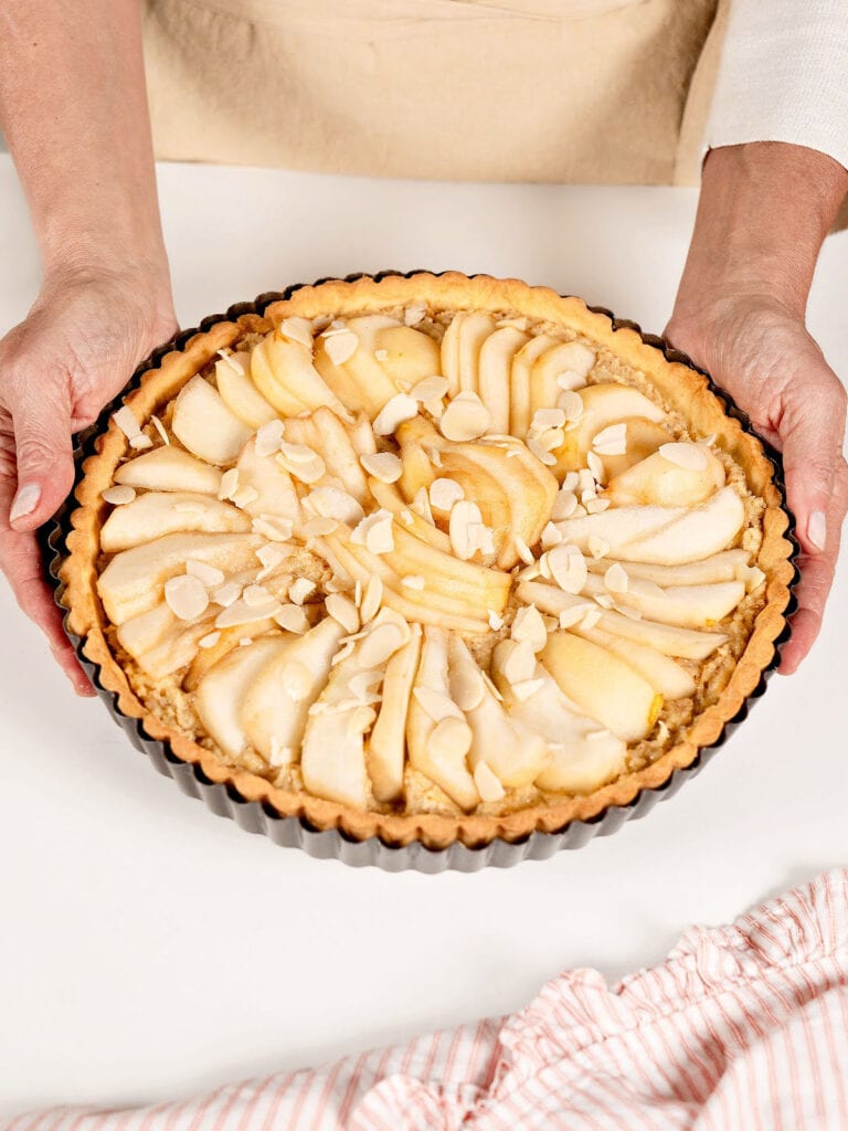 Holding pear tart ready to bake. White background.