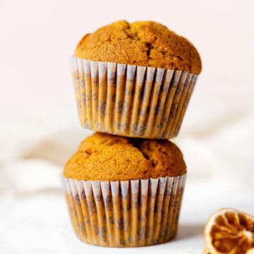 Close up image of two stacked pumpkin muffins on a white surface with pink background.