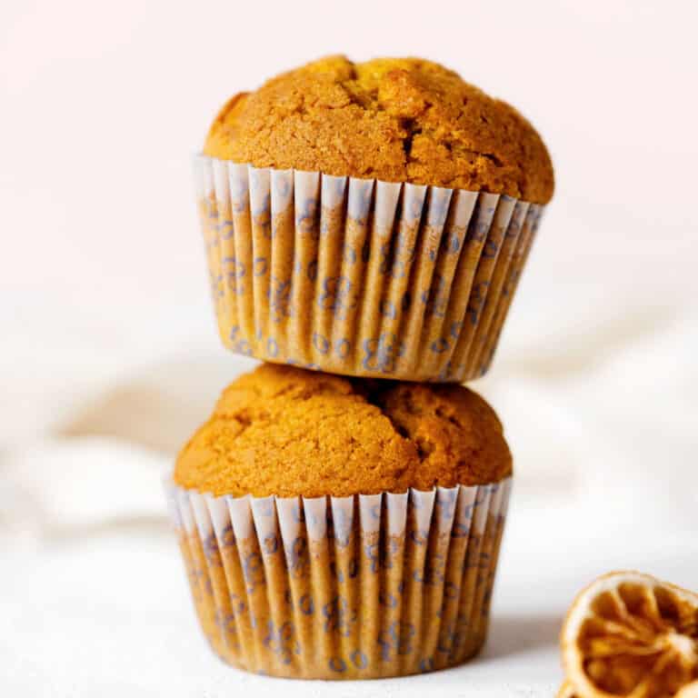 Close up image of two stacked pumpkin muffins on a white surface with pink background.