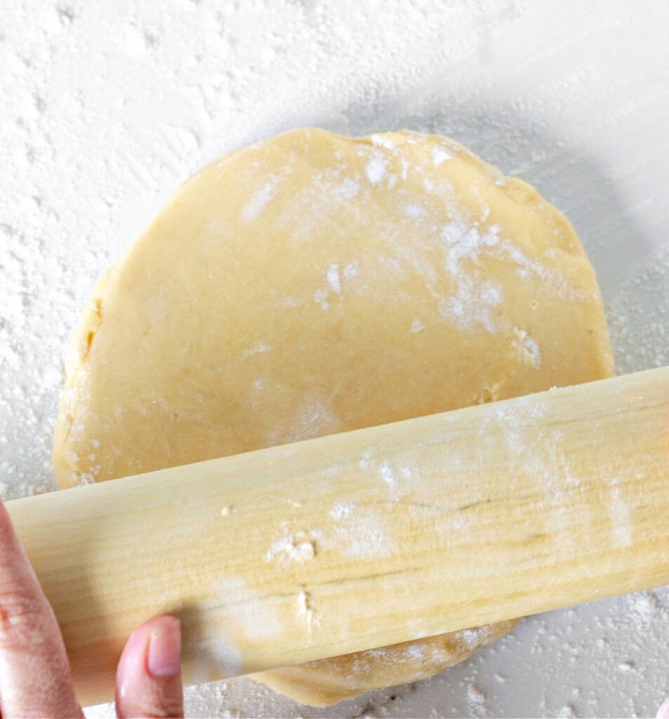 Rolling pie dough on a white surface. Rolling pin.