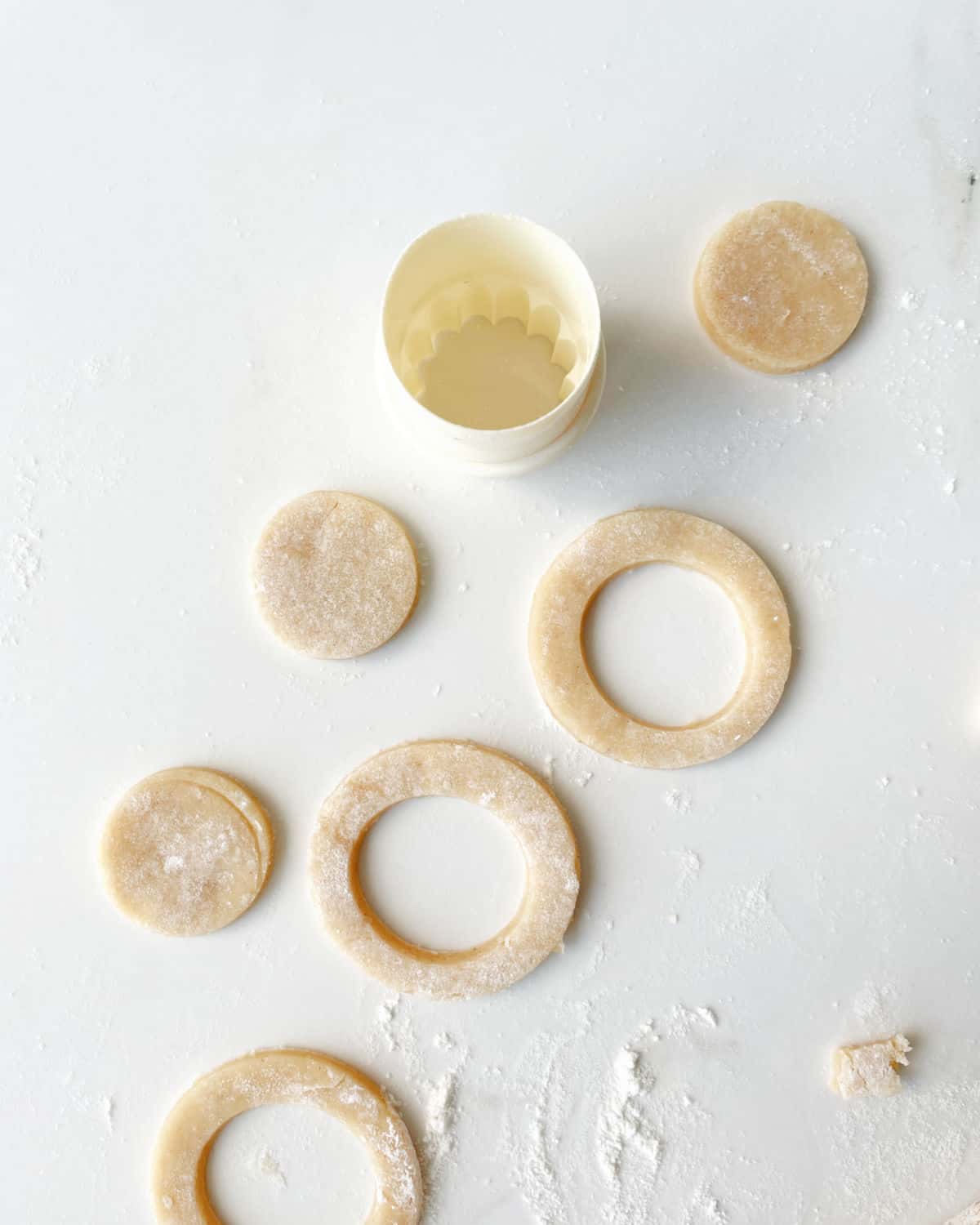 White surface with rounds of almond cinnamon cookie dough. A round plastic white cookie cutter.