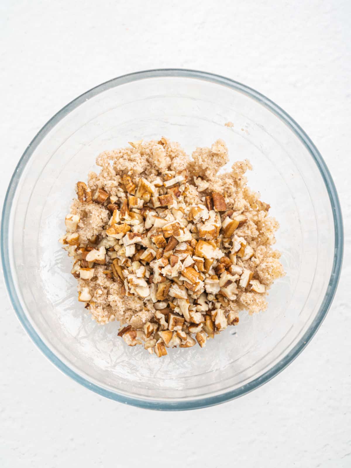 Streusel topping with pecans in a glass bowl on a white surface. Top view.