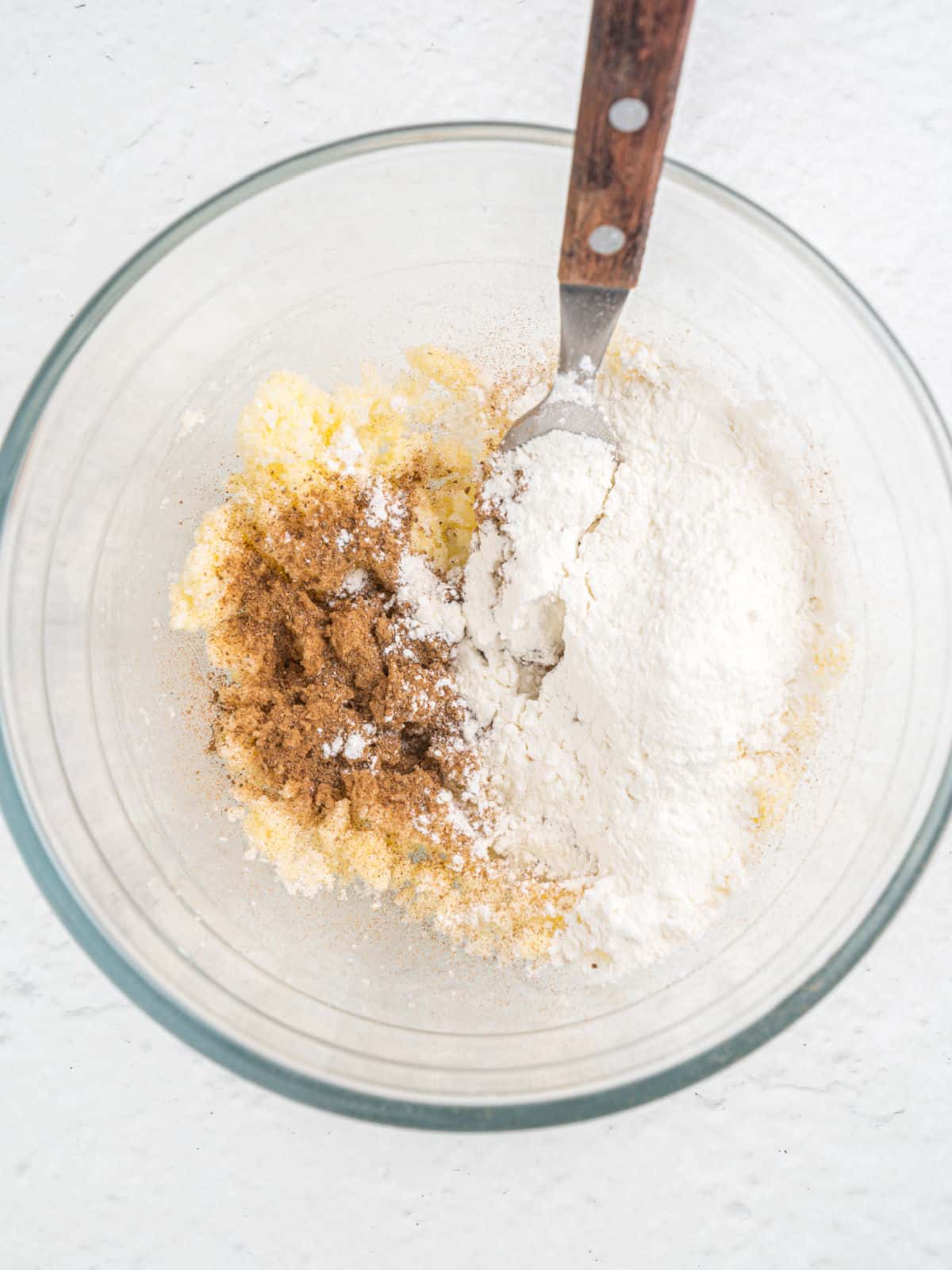 Mixing butter, flour, and brown sugar with a fork in a glass bowl on a white surface.