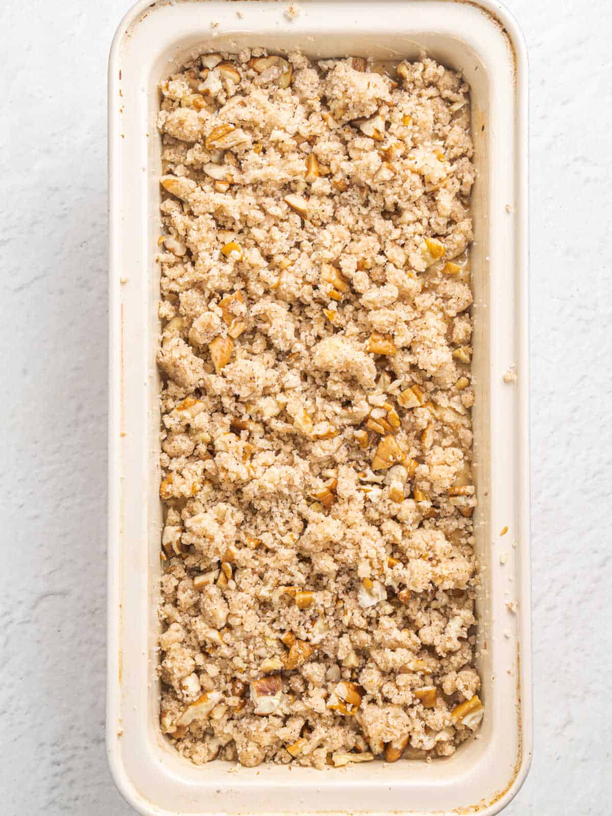 Top view of loaf pan with streusel topped bread batter on a white surface.