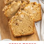 Red and brown text overlay on close up image of slices of streusel topped apple bread on a wooden board.