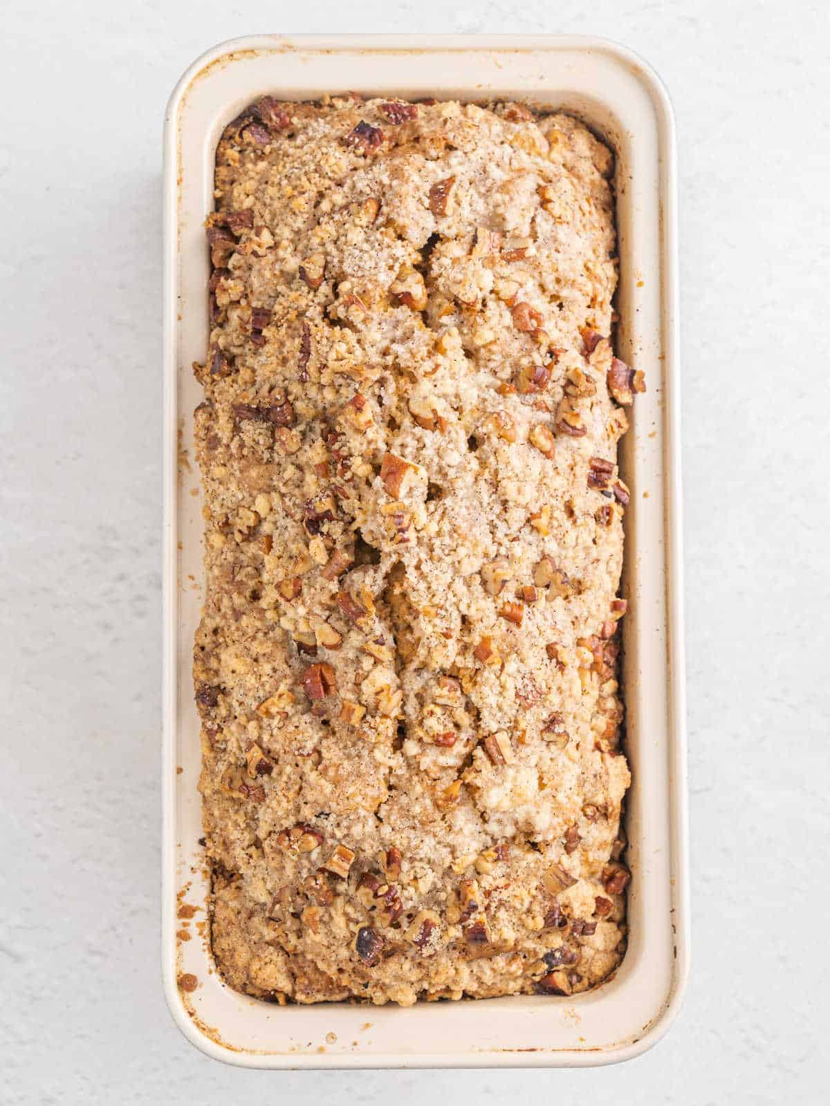Baked apple streusel bread on a light colored loaf pan on a white surface. View from above.