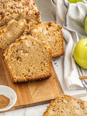 Streusel topped apple bread slices on a wooden board. White surface with cloth and green apples.